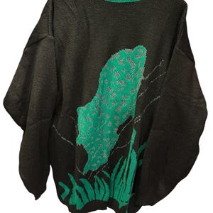 Può includere: Maglione nero con un design verde e grigio. Il maglione ha un colletto verde e un grande design verde sul davanti. Il design sembra essere una pianta o una foglia stilizzata.