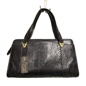 Op de afbeelding: Zwarte leren handtas met gouden hardware en een label met de tekst "Creazioni in pelle".