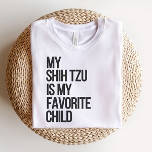 May include: White t-shirt with black text that reads "My Shih Tzu is my favorite child."