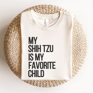 May include: A white t-shirt with black text that reads "My Shih Tzu is my favorite child."