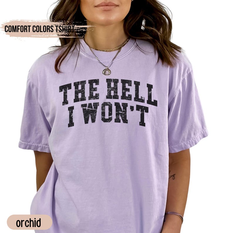 May include: A light purple t-shirt with the text "THE HELL I WON'T" printed in black. The shirt is a relaxed fit and has a crew neck.