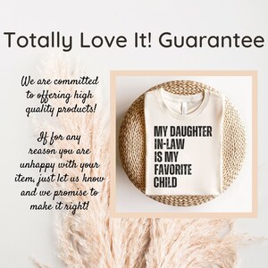 May include: A beige t-shirt with the text "My daughter in-law is my favorite child" printed in black. The shirt is displayed on a woven straw surface.