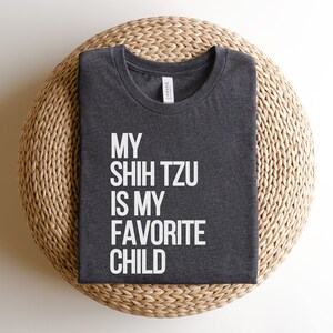 May include: A dark gray t-shirt with the text "My Shih Tzu is my favorite child" printed in white.