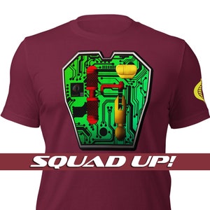 Könnte beinhalten: Ein maroonfarbenes T-Shirt mit einem grünen Schaltkreisdesign auf der Vorderseite. Das Design enthält eine Vielzahl kleiner, bunter Objekte. Das Shirt hat auch ein kleines gelbes Schlangenlogo auf dem rechten Ärmel. Der Text "SQUAD UP!" ist unter dem Design gedruckt.