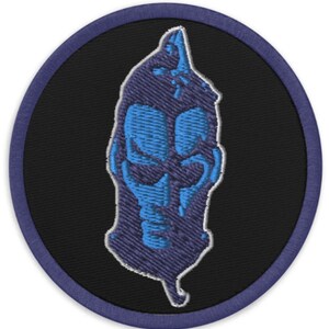 Puede incluir: Un parche bordado azul y blanco con un diseño de calavera. La calavera está bordeada de blanco y tiene una cara azul con una nariz y una boca blancas.