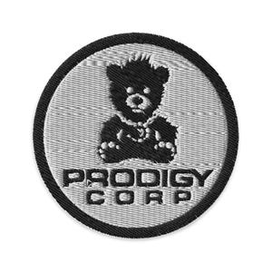 Op de afbeelding: Geborduurde patch met een zwart berenontwerp in een witte cirkel, omlijnd door een zwarte rand. De tekst "PRODIGY CORP" staat in zwarte blokletters onder de berenillustratie. De patch heeft een getextureerd uiterlijk.