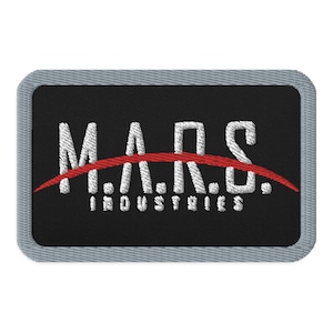 May include: A black and white embroidered patch with a red arc. The patch features the text "M.A.R.S. INDUSTRIES" in white.