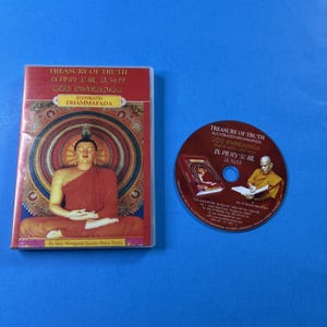 May include: A red DVD case and a CD with the text "TREASURY OF TRUTH ILLUSTRATED DHAMMAPADA" in multiple languages. The DVD case features an illustration of Buddha in a meditative pose. The CD has an image of a monk.