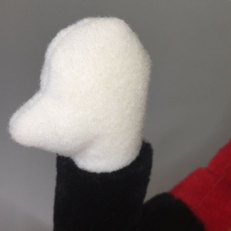 May include: A white plush hand with black and red fabric visible in the background.