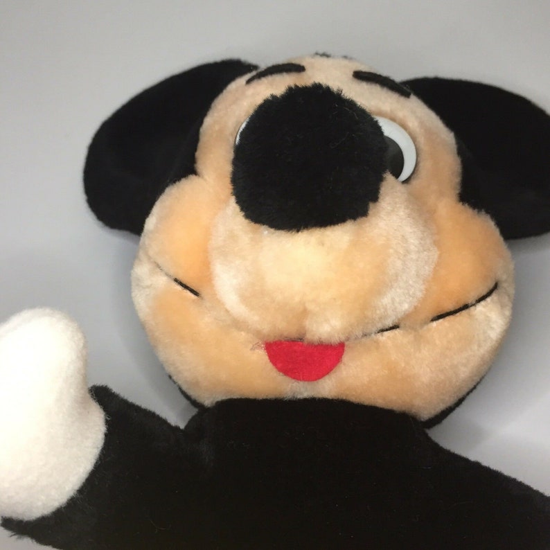 May include: A plush Mickey Mouse toy with black ears, a black nose, and a red tongue. The toy is made of soft, fuzzy fabric and has a friendly expression.