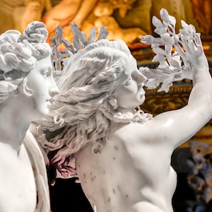 May include: A white marble sculpture of two figures, one with flowing hair and the other holding a branch of leaves. The sculpture is set against a background of ornate gold and blue details.