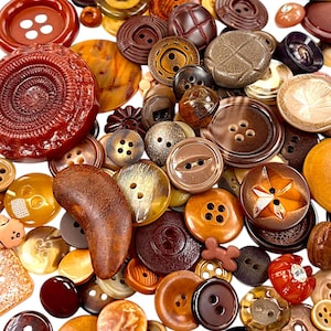 May include: A collection of various brown buttons in different shapes and sizes. The buttons include round, star, and textured designs, with two-hole and four-hole styles. The color palette ranges from light tan to dark brown, with some buttons having a marbled appearance.
