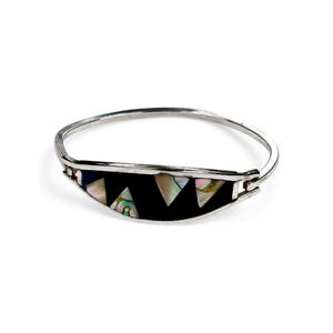Peut inclure: Un bracelet jonc argenté avec une incrustation noire ornée de coquillages irisés et d'éléments triangulaires. Le bracelet est doté d'un fermoir à charnière et d'un design incurvé.
