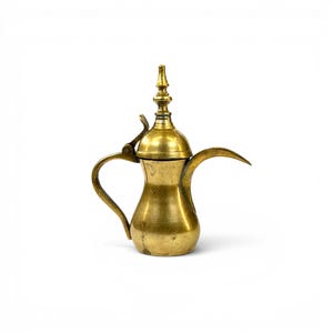May include: A brass coffee pot featuring a bulbous body, a long curved spout, and a hinged lid topped with a pointed finial. The metal surface displays a weathered, golden-toned patina with visible signs of age and use throughout the exterior.