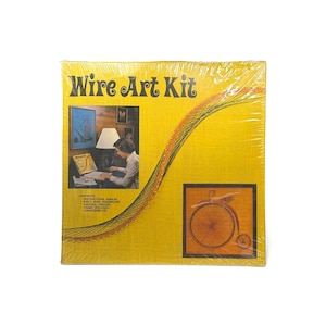 May include: A yellow Wire Art Kit box featuring the text Wire Art Kit, an illustration of a person working on a project, and a finished example of a penny-farthing bicycle design created with string on a board, all encased in clear plastic wrap.