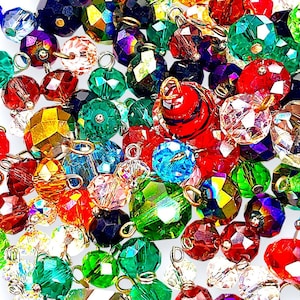 May include: A collection of faceted crystal beads in various colors, including red, green, blue, and yellow. Each bead has a metal loop for stringing. The beads are arranged closely together, creating a sparkling effect.