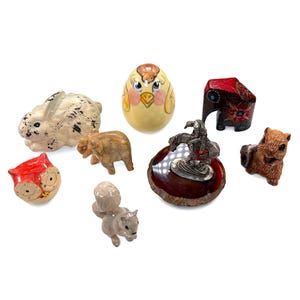 Puede incluir: Una colección de pequeñas figuras de animales, incluyendo un conejo, un búho, un elefante, una ardilla, un pájaro y un elefante tallado. Las figuras están hechas de varios materiales y presentan diseños y colores detallados.