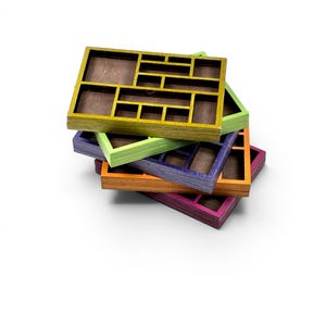 May include: A stack of five rectangular wooden organizer trays with multiple compartments. Each tray features a distinct colored frame in yellow, light green, purple, orange, and magenta, with a dark brown interior base for each section.