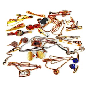 May include: A collection of vintage tie clips and cufflinks in gold, silver, and black. The assortment includes various designs, such as bars, chains, and novelty shapes. Some pieces feature decorative elements like chains and colored accents.