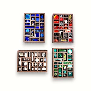 Puede incluir: Cuatro cajas de exhibición de madera llenas de varias cuentas de vidrio de colores y objetos decorativos. Las cajas contienen artículos azules, rojos, blancos y verdes, incluyendo formas geométricas, diseños florales y otras piezas únicas.