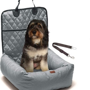 May include: A gray quilted dog car seat with a black leash attached. A dog is sitting in the seat.