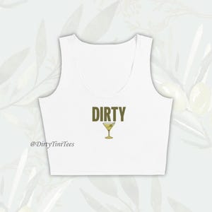 May include: White crop top with the text "DIRTY" in olive green and a martini glass graphic. The text "@DirtyTiniTees" is in the bottom left corner.