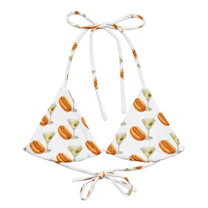 May include: A white bikini top featuring a repeating pattern of hot dogs and martini glasses with olives. The garment has triangular cups, thin white fabric ties at the neck, and a matching tie closure at the base for a secure fit.