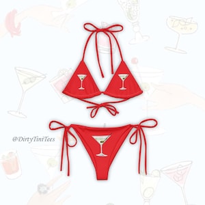 May include: Red bikini set featuring a triangle top and tie-side bottoms. Each piece has a martini glass graphic. The bikini is made of a smooth fabric and is designed for swimwear. The brand name "@DirtyTiniTees" is visible.