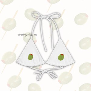 Könnte beinhalten: Weißer Dreiecks-Bikini-Oberteil mit grünen Oliven, die auf jeder Seite bedruckt sind. Das Bikini-Oberteil hat verstellbare Träger und Bänder am Rücken. Der Text '@DirtyTiniTees' ist auf der Vorderseite des Bikini-Oberteils aufgedruckt.