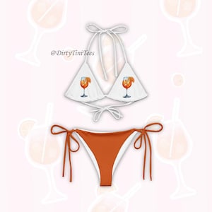 Może przedstawiać: Biały top od bikini i spód od bikini w kolorze spalonej pomarańczy. Top ma wiązanie na szyi i nadruk pomarańczowego koktajlu w szklance. Dół ma wiązane boki. Widoczny jest tekst "@DirtyTiniTees".