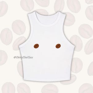May include: White crop top with two brown coffee bean designs on the front. The text '@DirtyTiniTees' is printed below the designs.
