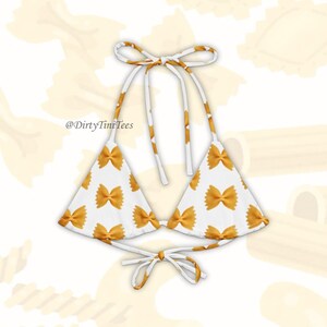 May include: A white triangle bikini top with a pattern of yellow farfalle pasta. The top has adjustable straps and ties at the back. The text '@DirtyTiniTees' is printed on the top.
