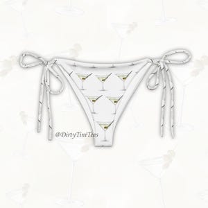May include: White bikini bottoms with a repeating pattern of martini glasses, each with an olive. The bikini has tie sides with black and white striped strings. The text "@DirtyTiniTees" is visible.