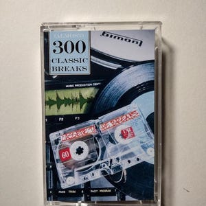 May include: A clear cassette tape case featuring the text "(ALMOST) 300 CLASSIC BREAKS" in blue and white. The case contains two cassette tapes and a record. The cassette tapes have the text "CASSETTE TAPE BREAKS" and "UR" printed on them.