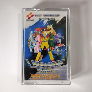 May include: A vintage Konami "Lagrange Point" Famicom OST cassette tape. The cover art features a group of anime characters in vibrant colors against a blue and white space background. The cassette is in a clear plastic case.