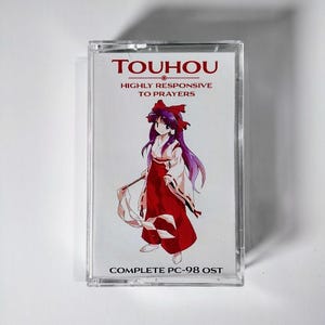 May include: A Touhou cassette tape with a vibrant illustration of a character in a red and white outfit and purple hair. The text on the cassette reads "TOUHOU HIGHLY RESPONSIVE TO PRAYERS COMPLETE PC-98 OST."