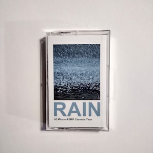 May include: A clear plastic cassette tape case with a white label. The label has a blue and white image of rain and the text "RAIN 60 Minute ASMR Cassette Tape".