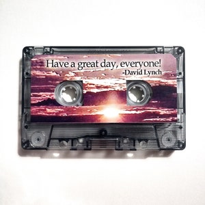 May include: A clear cassette tape with a sunset image and the text "Have a great day, everyone! -David Lynch" printed on the front.