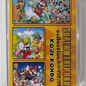 Può includere: Una cassetta della collezione Super Mario Bros. con illustrazioni colorate di Mario e altri personaggi. La cassetta è in una custodia di plastica trasparente con testo giallo e nero.