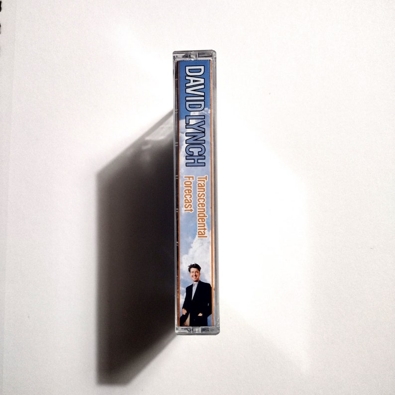 May include: A cassette tape with a blue and white background. The text "Transcendental Forecast" is printed in orange on the tape. The name "DAVID LYNCH" is printed in blue on the tape. A man in a suit is pictured on the tape.