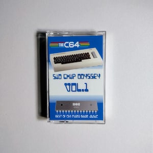 May include: A cassette tape with a blue and white label. The label features a picture of a Commodore 64 computer and the text "SID Chip Odyssey Vol. 1 Best of C64 Video Game Music".