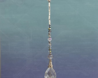 May include: A clear crystal teardrop pendant with a silver-colored metal cap and a strand of clear and iridescent beads. The pendant hangs from a thin silver-colored chain, creating a delicate and elegant design.