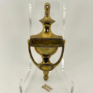 Peut inclure: Un heurtoir de porte en laiton en forme d'urne avec une plaque rectangulaire. Le heurtoir est monté sur un support en acrylique transparent et comprend deux vis pour l'installation.