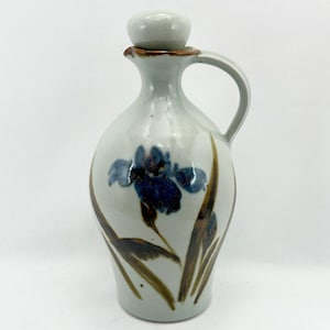 May include: A white ceramic jug with a brown glaze and a blue and purple floral design. The jug has a round body and a spout with a lid.