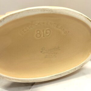 May include: Close-up of the base of a Beswick Ware ceramic piece. The base is oval-shaped and a light beige color. The text "Beswick - England" and the number "819" are embossed on the base. The words "Beswick Ware" and "Made in England" are also visible.