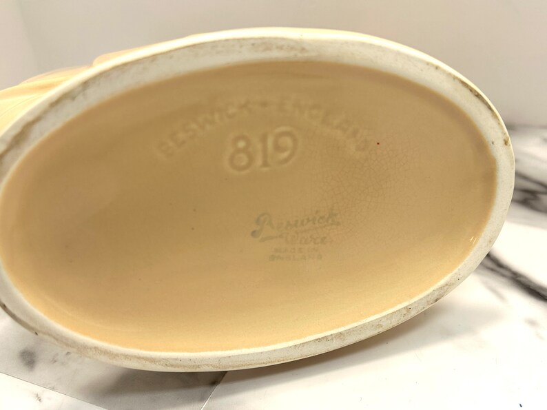 May include: Close-up of the base of a Beswick Ware ceramic piece. The base is oval-shaped and a light beige color. The text "Beswick - England" and the number "819" are embossed on the base. The words "Beswick Ware" and "Made in England" are also visible.