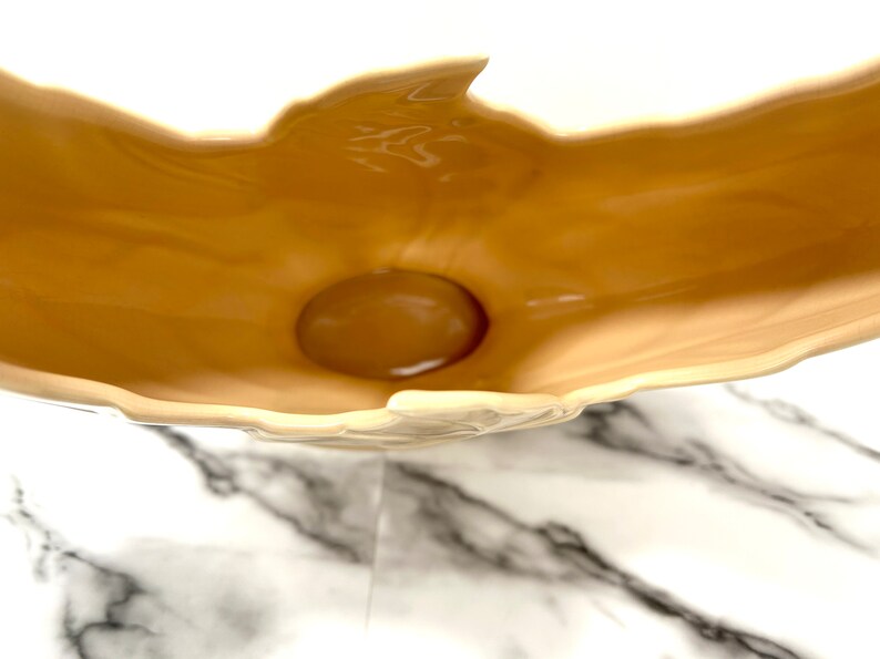 May include: A beige ceramic decorative bowl with a glossy finish. The bowl has a unique, organic shape with a rounded base and a raised, petal-like rim. The interior is a darker shade of beige than the exterior.