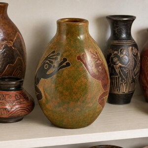 Peut inclure: Collection de vases en céramique faits à la main de différentes tailles et couleurs. Le vase central est vert olive avec des motifs en forme de mains noires et rouges. D'autres vases sont bruns et noirs, certains avec des motifs sculptés.