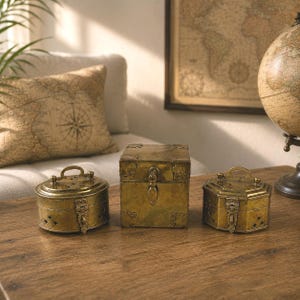 Peut inclure: Un ensemble de trois boîtes de rangement en laiton au fini métallique vieilli. La collection comprend une boîte ovale, une boîte carrée et une boîte hexagonale, chacune dotée d'un couvercle à charnière, d'un loquet décoratif et d'une poignée.