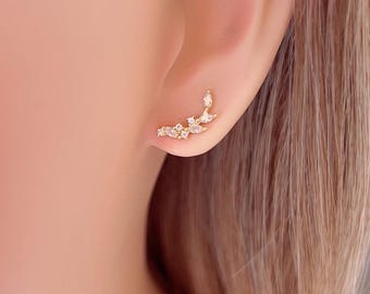 May include: A gold ear cuff with a delicate design of small, clear cubic zirconia stones arranged in a curved shape. The ear cuff is worn on the upper part of the ear.